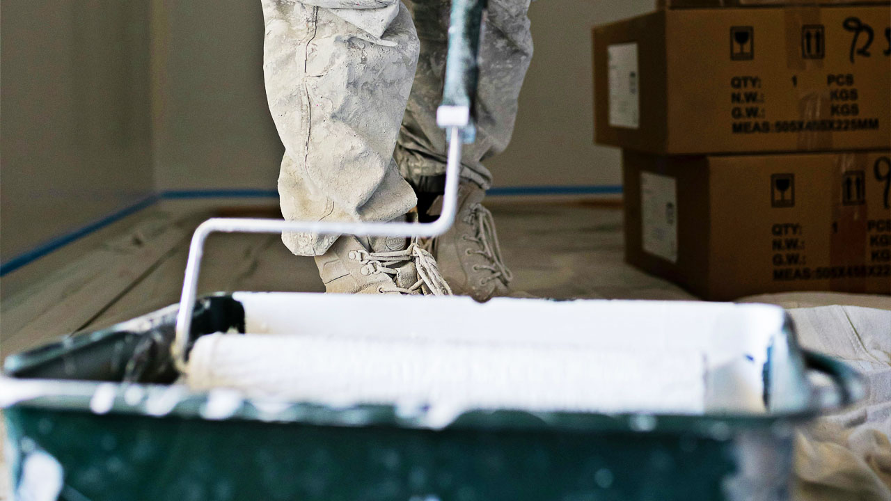 Someone putting white paint onto a roller Someone putting white paint onto a roller