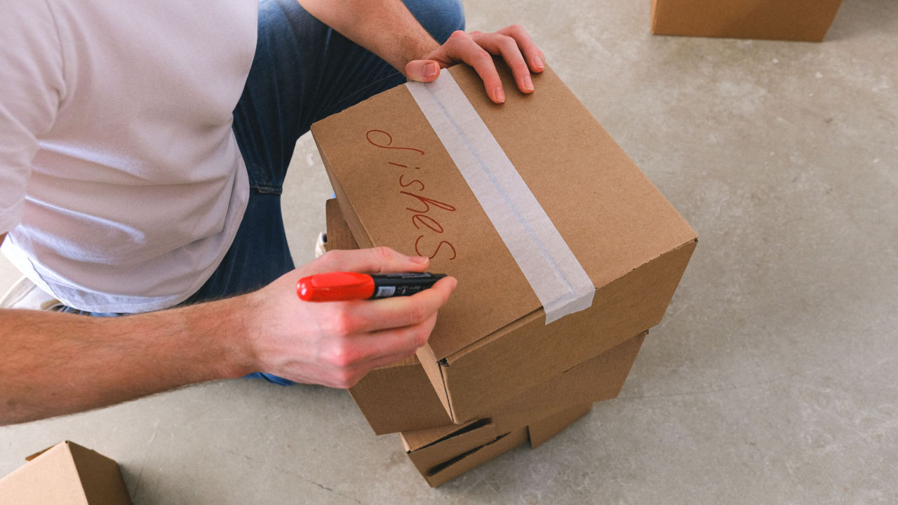 A Man Writes The Contents of a Moving Box on The Top